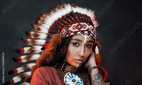 Plakat Studio portrait of a beautiful American Indian girl with tattoo on hand in colorful traditional ethnic costume on a dark background