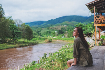 Portrait image of a beautiful asian woman sitting by the river with mountains and nature background