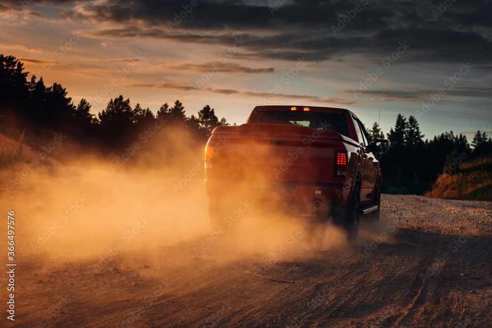 Pickup truck in motion on a country road with clouds of dust. An SUV is driving fast during sunset on a rural gravel road with a lot of dust. fast moving car