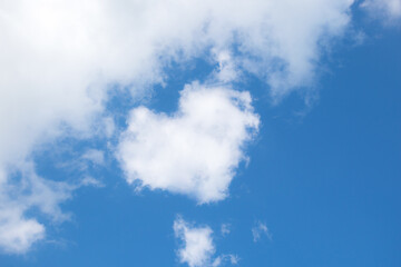 Wall Mural - Fluffy white clouds float across the blue sky on a clear sunny summer or spring day. Background sky. Heart shaped cloud. Low angle view