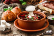 Ukrainian and Russian traditional beetroot soup or borscht in bowl with rib eye meat, buns, parsley on wooden rustic background. Hand pours sour cream from spoon in beet soup. Healthy food, close up
