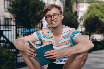 Smiling student with glasses and with books outside. Portrait of a happy young man