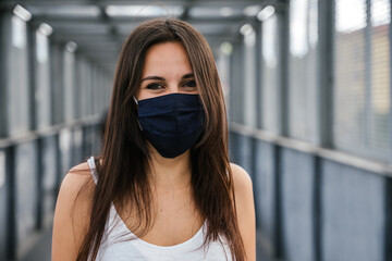 Portrait of beautiful woman on iron bridge in the summer in the city with face mask for protection from contagion by Coronavirus, Covid-19 - Millennial looking and smiling - Concept of naturalness