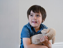 Portrait Happy Boy Playing With Dog Toy On White Background, Adorable Child With Big Smile Playing With Soft  Toys Relaxing At Home. Positive Children Concept