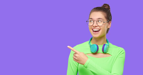 Horizontal banner of girl in green top and glasses, pointing left to copy space, feeling excited, isolated on purple background