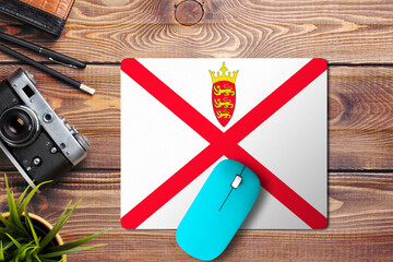 Wall Mural - Jersey flag on wooden background with blue wireless mouse on a mouse pad, top view. Digital media concept.