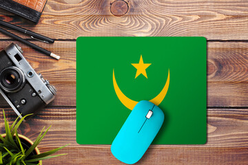 Wall Mural - Mauritania flag on wooden background with blue wireless mouse on a mouse pad, top view. Digital media concept.