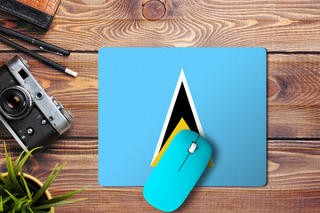 Wall Mural - Saint Lucia flag on wooden background with blue wireless mouse on a mouse pad, top view. Digital media concept.