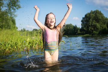 a little girl in a bathing suit jumps and splashes water in the lake in summer