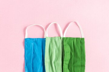 Poster - Closeup shot of blue, light green, and dark green protective face masks on a pink background