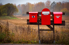 Three Red Mailboxes In The Countryside Near An Autumn Field