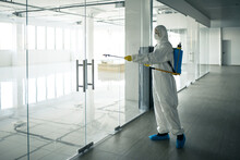 Sanitary Worker Sprays An Empty Business Center With Antiseptical Liquid To Prevent Covid-19 Spread. A Man Wearing Disinfection Suit Cleaning Up The Shopping Mall. Nobody, Health, Isolated Concept.