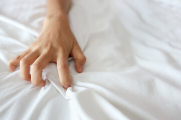 Close up young sexy woman hand pulling white sheets in ecstasy in hotel. Cute girl doing sign orgasm on white bed (sex and erotic concept for advertisement)