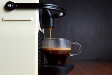 Espresso machine making coffee with capsules in a glass cup on wooden table. Front view. Copy space. Selective focus..