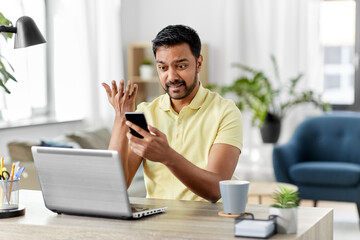 Poster - technology, remote job and failure concept - angry indian man with smartphone and laptop computer at home office