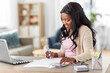 © Syda Productions - remote job, technology and people concept - happy smiling young african american woman with calculator and papers working at home office