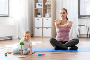 family, sport and motherhood concept - happy smiling mother exercising on mat and little baby playing with toys at home