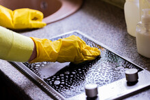 Close Up View Of Person In Yellow Rubber Gloves Cleaning Kitchen, Removes Tough Grease Grime, Washes, Wipes Induction Stove With Microfiber Cloth. Housework Cleaning Service, Household Chores