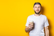 © Alex - Friendly young man holding a paper cup of coffee on yellow background.