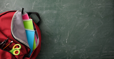 Backpack full of school supplies on green blackboard top panoramic