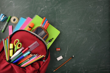 Backpack full of school supplies on green blackboard top view