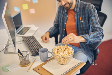 Cheerful young man eating popcorn at work