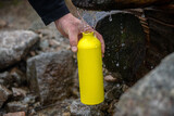 Fototapeta  - turysta napełniający żółtą metalowa butelkę wodą