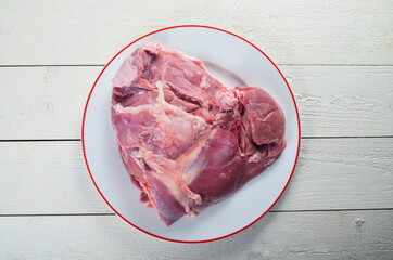 Fresh raw meat turkey thigh bone on a white plate and white wooden background, horizontal