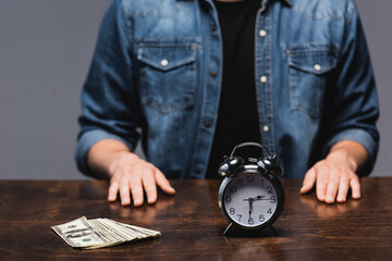 Wall Mural - Selective focus of dollars and alarm clock on table near man isolated on grey, concept of time management