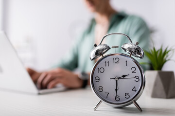 selective focus of alarm clock on table near man using laptop at home, concept of time management