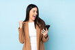 © luismolinero - Young caucasian woman isolated on blue background with phone in victory position
