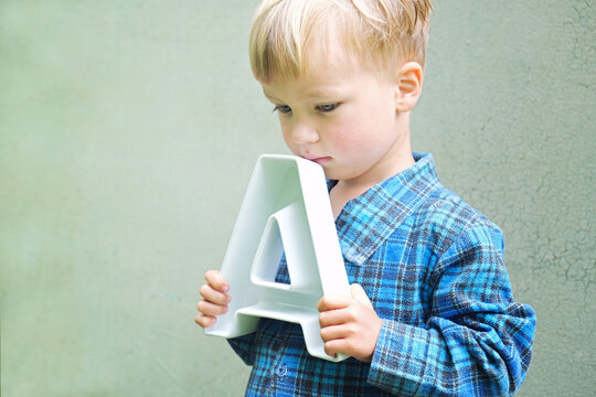 Sad preschool child holding big letter A and thinking. Back to school, learning alphabet, education concept.