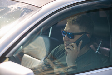 Wall Mural - Driver is talking on mobile phone by a steering wheel of car.