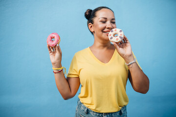 Portrait of a girl in yellow t-shirt eating donuts at blue wall