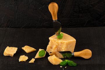 Wall Mural - Parmesan cheese on black background with knife and basil leaves