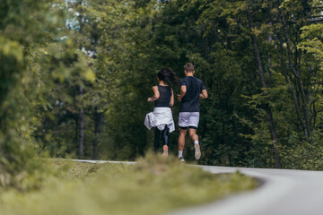 Young fit couple atheltes running on running road in a forest.