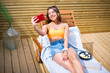 © Joe Urrutia/ADDICTIVE STOCK - From above positive female in shorts and bra lying on deck chair on sunny day and taking photo on camera of cellphone