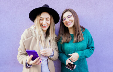 Portrait of two young friends using their mobile phone in violet background -  Lifestyle and friendship concepts