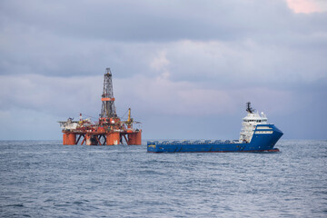 Wall Mural - Offshore Jack Up Rig And Supply Ship In The Middle of The Sea at Sunset Time