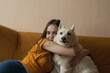 © bela_zamsha - The girl strokes and caresses a white West Siberian husky Laika dog, which lies on a yellow sofa, sticking out a long tongue