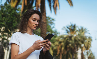 Wall Mural - pretty woman writes message on mobile smartphone while walking Park barcelona on a warm summer day, hipser girl listens to music on earphones and searches for information using cell phone