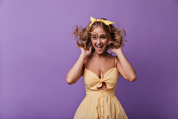 Wall Mural - Stunning woman with bronze skin jumping on purple background. Indoor photo of cute smiling girl with blonde curly hair.