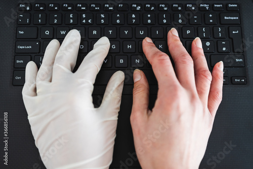 hand typing on shared computer keyboard at work wearing disposable glove to avoid contact with potentially infected surfaces and other hand without glove