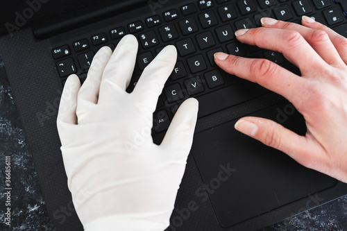 hand typing on shared computer keyboard at work wearing disposable glove to avoid contact with potentially infected surfaces and other hand without glove