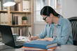 Female student taking notes from book at home. Young asian japanese woman sitting at table doing assignments for final exam project at school. side view of smart elegant college girl doing homework.