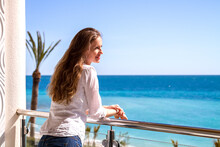 The Beautiful Woman Standing On A Balcony Of Apartments Looking At The Seaside.
