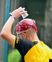  Man, An Athlete With A Scarf On His Head Pours Water From A Plastic Glass On Himself In The Heat