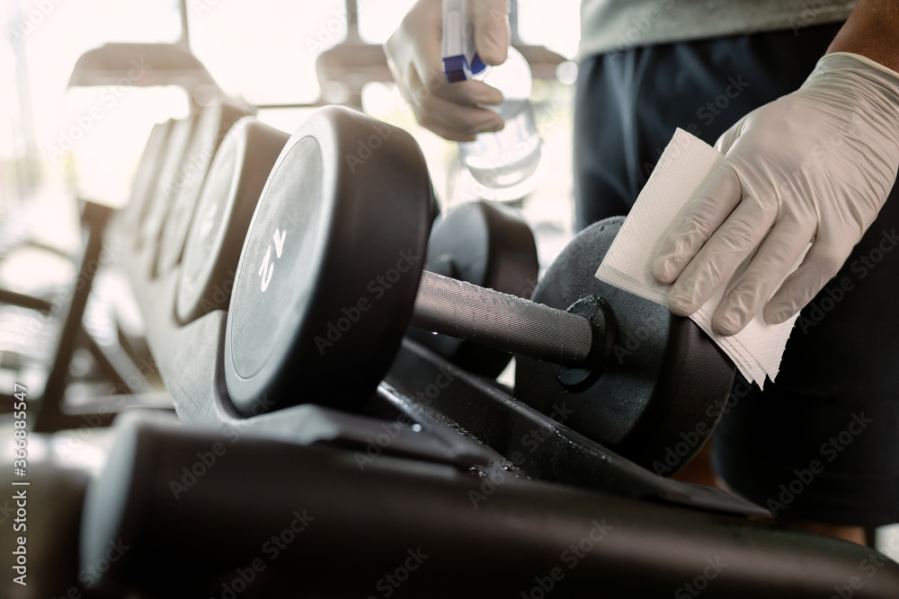 Close-up of athlete disinfecting hand weights in a gym. - obrazy, fototapety, plakaty 