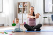 family, sport and motherhood concept - happy smiling mother exercising on mat and little baby playing with toys at home
