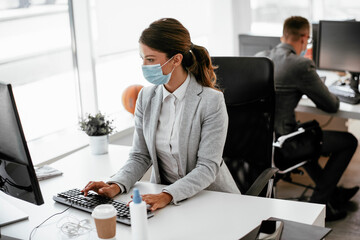 Beautiful businesswoman with medical mask working in office. Young businesswoman working on lap top.	